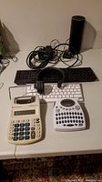 Photo showing the full set of items including two keyboards (one black missing a key and one white), a headset, Dymo label maker, calculator, Apple TV and Amazon Echo.