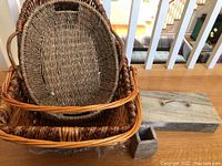 Three woven baskets stacked inside each other, showing oval and rectangular shapes, along with two bathroom storage containers - a rectangular box with a handle and a small square container on the side.