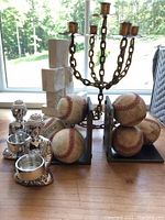 A full view of the lot items on a table near window showing the brass four-arm candle holder, baseball bookends, silver-colored holders, and onyx decoration.