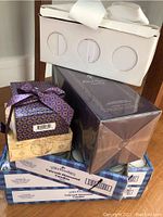 Multiple boxed items stacked: boxed Robert Graham Valour fragrance set, Glass Baby candle holders in original packaging, and three boxes of Yahrzeit memorial candles.