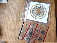 Buckingham Palace commemorative coin with floral border and text in sealed protective clear packaging, laid on wood surface with other loose coins in packaging strips