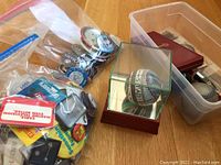 Two bags of assorted buttons and pins, a Yankees commemorative baseball in glass case, and a watch box placed on a wooden surface.