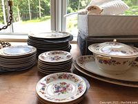 Photo showing stacks of plates, bowls, cups, and a lidded dish with floral pattern and gold trim.