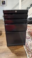 Front view of black metal file cabinet with four drawers, lock present but no key.