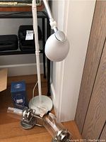 Photo showing white metal floor lamp with adjustable arm and spherical lamp head, along with hurricane lanterns placed near its base