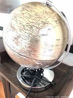 Photo showing the globe's upper hemisphere and its geographical details including parts of Asia with a silver metal base and electrical cord wrapped around it.