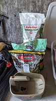 Photo showing Safe Step Ice Melter, Bayer insect control, Quick Grow grass seed bags, and Scotts Wizz spreader's handle and part of container.