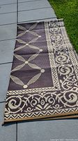 Photo showing corner of the rug laid out on a patio with the darker side up displaying geometric and floral pattern in brown and beige.