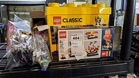 Yellow Lego Classic storage box with some smaller Lego boxes in front and bags of loose pieces around
