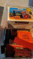 Mamod steam tractor boxed with an image of the tractor labeled SE1, a Lionel Trainmaster Transformer box and some train accessories visible in a plastic storage container.