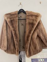 Close-up image of a light brown mink fur coat on a hanger showing plush fur texture and patterned inner lining.