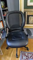 Front view of black mesh back office chair with cushioned seat and armrests showing wear