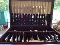 Full view of the flatware set neatly stored in a wooden box with velvet lining, showing knives, forks, and spoons.