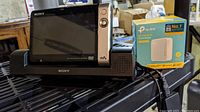 Sony portable DVD player on black plastic surface with charging station and TP-Link AC750 router next to it.