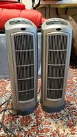 Two matching Lasko tower space heaters placed side by side on a patterned carpet.