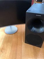 Front view of Samsung curved color display and black Samsung subwoofer on a wooden floor.