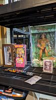 Photo showing the Tarzan figurine in original packaging, two bobbing heads (RBG and Anna Nicole Smith), The Slum Gang playing cards, and GLO bracelets arranged on a shelf.