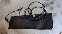 Photo of black rectangular heated mat with attached power cable and plug, showing mat surface and cable length.