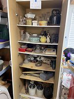 Full view of cabinet shelves showing various vintage decor items including glassware, bronze figurine, crock jugs, books, and antiques.