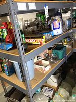 Shelves filled with cleaning products including sprays, powders, garbage bags, and kitchen items such as glassware and light bulbs.