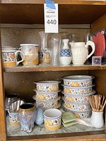 Full shelf view showing stacked Dansk bowls with fruit and floral patterns, Wedgwood pitcher, various glass vases, and additional small items including glazed cups and toothpicks.