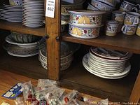 Shelf filled with Dansk china with fruit motif including bowls, mugs, serving dish, and other plates.