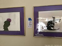 Two framed animation cels side by side on wall showing green head silhouette (left) and black dragon silhouette (right)