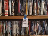 Full view of two wooden shelves filled with DVDs arranged side by side showing the front covers, including a MaxSold lot tag in the center middle of the image.