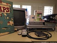 Wide angle photo showing the electronics lot including TV, players, remotes, book, and cables