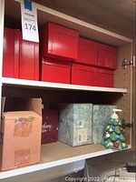 Shelf with six red Gorham Crystal boxes, gift bag, cardboard boxes, and a ceramic Christmas tree dispenser.