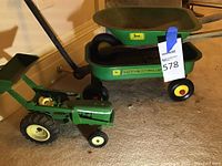Photo showing the green and yellow metal John Deere toy tractor and two-wheel wagon with wooden handle.