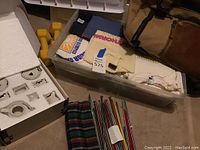 Overview of entire lot showing tea set box, dumbbells, t-shirts, knitting needles, duffel bag