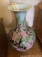 Photo showing a tall ceramic vase with a floral pink cherry blossom pattern on a light green background.