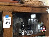 Display of clear glass pitcher, ribbed glass decanter with stopper, black and clear acrylic Mickey Mouse salt and pepper mills, and Mickey and Minnie Mouse salt and pepper shakers.