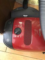 Top view of red canister base showing control dial, vent and Miele logo
