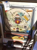 Front view of pachinko machine showing round playfield with pins, bumpers, shooter lever, and ball tray