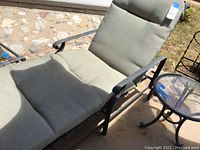 Chaise lounge with olive green cushion and black metal frame, showing armrest and cushion seating