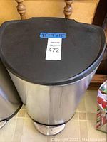 Closed view of stainless steel Simplehuman trash can with black lid and foot pedal, with measurement label on lid.