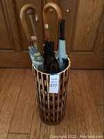 Umbrella holder with umbrellas inside, showing wooden slat design and five umbrellas with wooden and black handles.