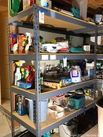 Full view of metal utility shelf loaded with various household items on four shelves under basement ceiling.