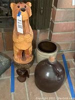 Standing wooden bear carving with a price tag, positioned next to a job jar and smaller bird carving on tile floor.