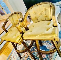 Two wooden bar stools with basket weave backs and beige tufted cushions on a floral rug