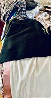 Photo showing a black women's skirt and white gown or dress on top of a bed among many clothes