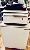 Photos of Harris 3M 6010 copier sitting on matching cabinet stand, displayed from two angles showing condition and branding