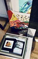 Colorful abstract painting on canvas leaning against the wall with several other framed prints stacked below it