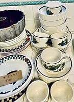 Photo showing stacked Temperware by Lennox coffee cups, saucers, bowls and plates with floral design, a bundt cake pan, and checkered patterned plates and bowls.