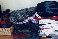Folded men's clothing items including shirts on top with graphic prints, plaid pajama pants beneath, and slacks.