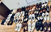 Multiple pairs of men's shoes arranged on the floor, showing various colors and styles including dress and casual shoes.