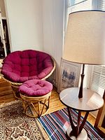 Photo shows the red papasan chair with matching ottoman alongside the mid-century wood table lamp on a round wood table.