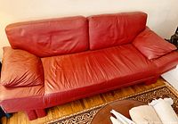 Red leather couch seating for three with visible creases and slight wear.